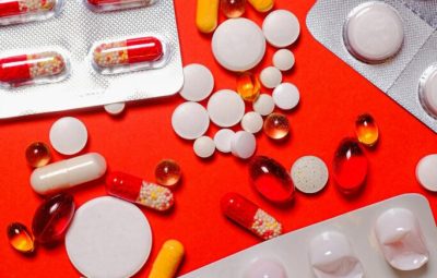 An assortment of colorful pills and capsules scattered on a vibrant red background